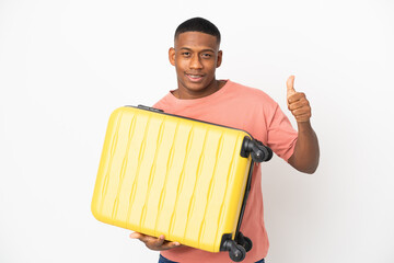 Young latin man isolated on white background in vacation with travel suitcase and with thumb up