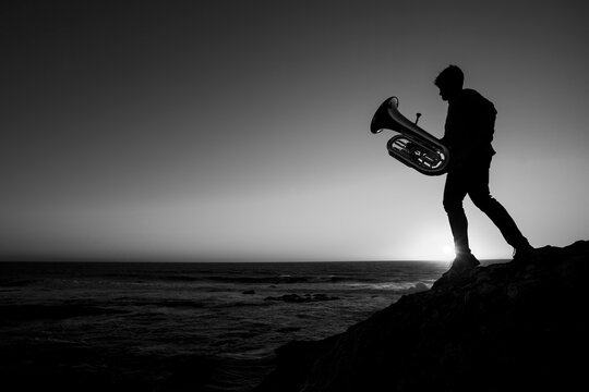 Silhouette of a musician with a tuba on the seashore. Black and white photo.