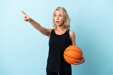 Young Russian woman playing basketball isolated on blue background pointing away