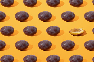 Arranged plum and one half on orange background. Minimal design and pattern.