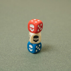Arranged dice red, blue and white with skull and number six one on top of the other on green background. Minimal design.