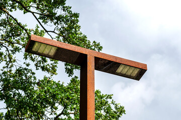 Fototapeta premium A metal rusty street lamp, against a cloudy sky, visible trees.