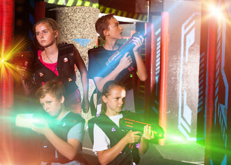Cheerful teen girls and boys with laser pistols posing together in dark laser tag labyrinth..