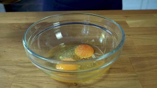 Female hands adds salt, pepper and olive oil into a bowl with cracked aggs. And whips with a fork. scrambled eggs making process. Close up