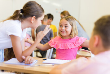 Fototapeta premium Schoolkids performing group tasks during lesson. Their teacher standing and observing.