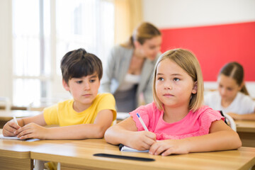 Fototapeta premium Schoolchildren doing test exercise during lesson. Boy cheating and looking in classmate's copy-book.