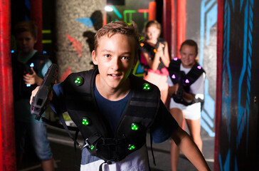 Emotional teen boy with laser pistol playing laser tag with friends on dark labyrinth..