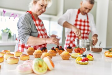 Senior caucasian couple smiling happy baking sweets at the kitchen.