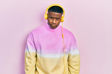 Young black man listening to music wearing headphones skeptic and nervous, frowning upset because of problem. negative person.