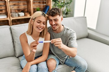 Young caucasian couple smiling happy holding pregnacy test at home.