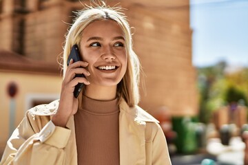 Young blonde girl smiling happy talking on the smartphone at the city.