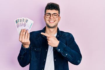 Young hispanic man holding egyptian pounds banknotes smiling happy pointing with hand and finger