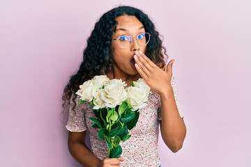 Young latin woman holding flowers covering mouth with hand, shocked and afraid for mistake. surprised expression