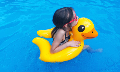 Cute girl in sunglasses swimming with rubber duck in swimming pool