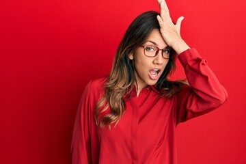 Young latin woman wearing casual clothes and glasses surprised with hand on head for mistake, remember error. forgot, bad memory concept.