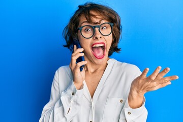 Young brunette woman having conversation talking on the smartphone celebrating achievement with happy smile and winner expression with raised hand