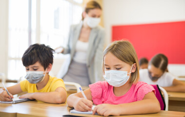 Portrait of schoolgirl in mask sitting in classroom during lesson in elementary school