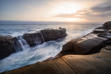 sunrise on the rocks at the coast with a waterfall