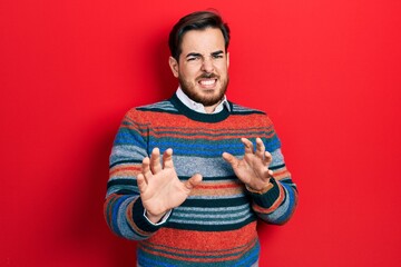 Handsome caucasian man with beard wearing elegant wool winter sweater disgusted expression, displeased and fearful doing disgust face because aversion reaction. with hands raised