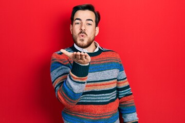 Handsome caucasian man with beard wearing elegant wool winter sweater looking at the camera blowing a kiss with hand on air being lovely and sexy. love expression.