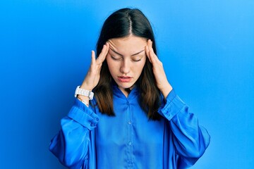 Young brunette woman wearing casual blue shirt with hand on head for pain in head because stress....