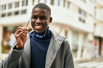 Young african american man smiling happy holding glasses at the city