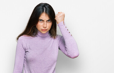 Young beautiful teen girl wearing turtleneck sweater angry and mad raising fist frustrated and furious while shouting with anger. rage and aggressive concept.