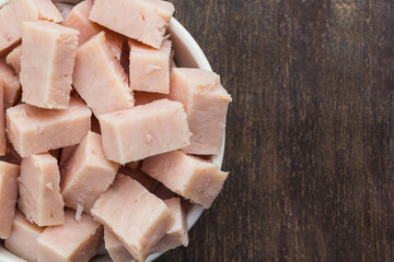 Turkey breast cubes in a white pot isolated on a wooden cutting board. Selective focus. Top view.