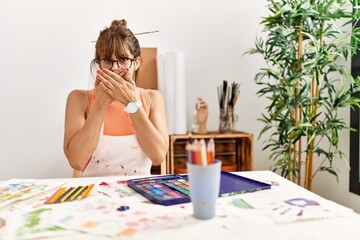 Hispanic woman at art studio shocked covering mouth with hands for mistake. secret concept.