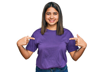 Young hispanic girl wearing casual purple t shirt looking confident with smile on face, pointing oneself with fingers proud and happy.