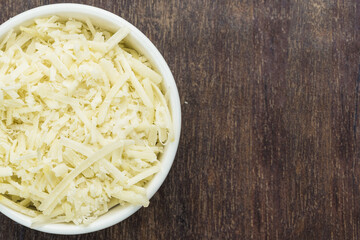 Grated cheese in a white pot isolated on a wooden cutting board. Selective focus. Top view.