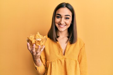 Young brunette girl holding bowl with spaghetti looking positive and happy standing and smiling with a confident smile showing teeth