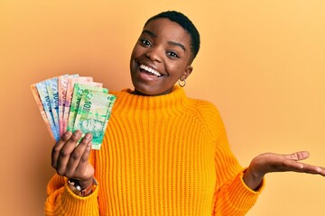Young african american woman holding south african rand banknotes celebrating achievement with...