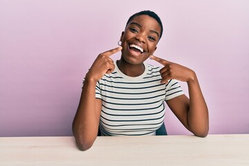 Young african american woman wearing casual clothes sitting on the table smiling cheerful showing...