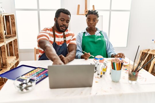 African american painter couple having online paint class sitting on the table at art studio