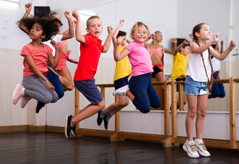 Fototapeta premium Group of happy sporty kids with female teacher training in modern dance studio, jumping together
