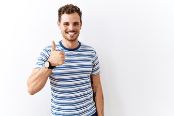 Handsome young man standing over isolated background doing happy thumbs up gesture with hand. approving expression looking at the camera showing success.