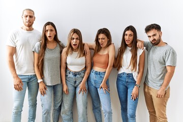 Group of young friends standing together over isolated background in shock face, looking skeptical and sarcastic, surprised with open mouth