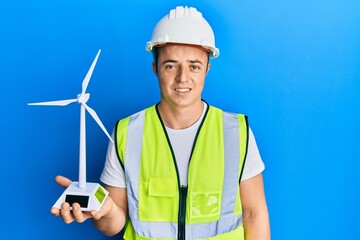 Handsome young man holding solar windmill for renewable electricity looking positive and happy standing and smiling with a confident smile showing teeth