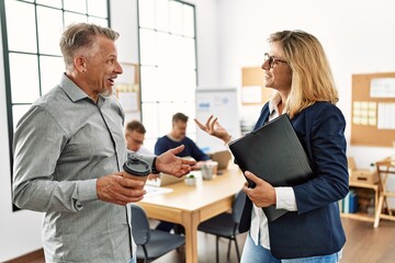 Two middle age business workers speaking while partners working at the office.