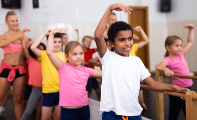 Group of boys and girls training along ballet bar at dance class