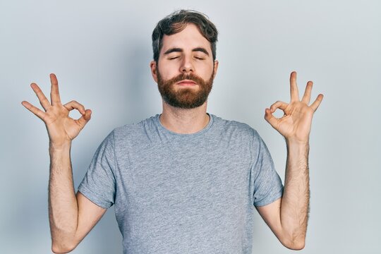 Caucasian man with beard wearing casual grey t shirt relax and smiling with eyes closed doing meditation gesture with fingers. yoga concept.