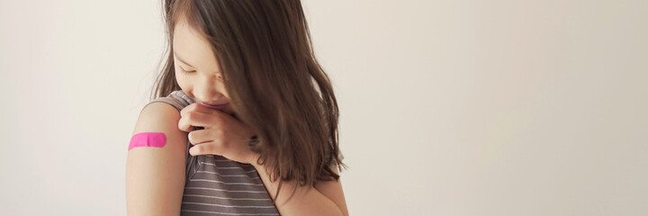 Mixed Asian young girl showing her arm with pink bandage after got vaccinated or  inoculation,...