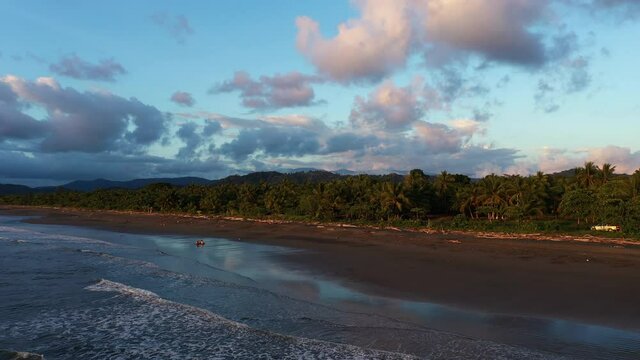 Sunset over black sand beach full of palm trees Zancudo Costa Rica paradise aerial