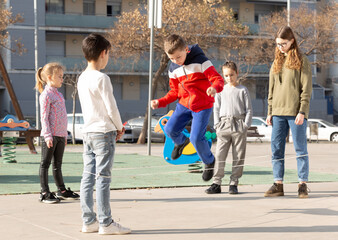 Fototapeta premium Energetic kids playing and skipping on elastic jumping rope in european yard. High quality photo