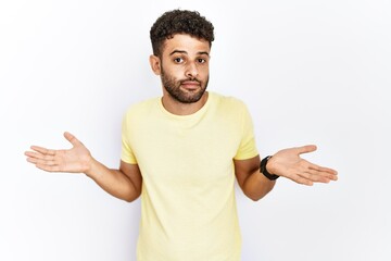 Arab young man standing over isolated background clueless and confused expression with arms and...