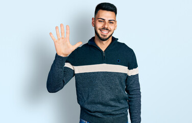 Young hispanic man with beard wearing casual winter sweater showing and pointing up with fingers number five while smiling confident and happy.