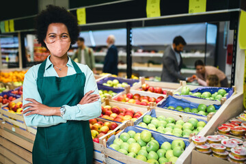 Portrait of African American female employee in grocery store. She is wearing protective face mask...