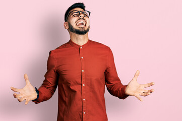 Young hispanic man with beard wearing business shirt and glasses crazy and mad shouting and yelling with aggressive expression and arms raised. frustration concept.