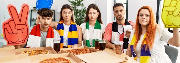 Group of young hispanic people eating pizza supporting soccer team at home thinking attitude and...